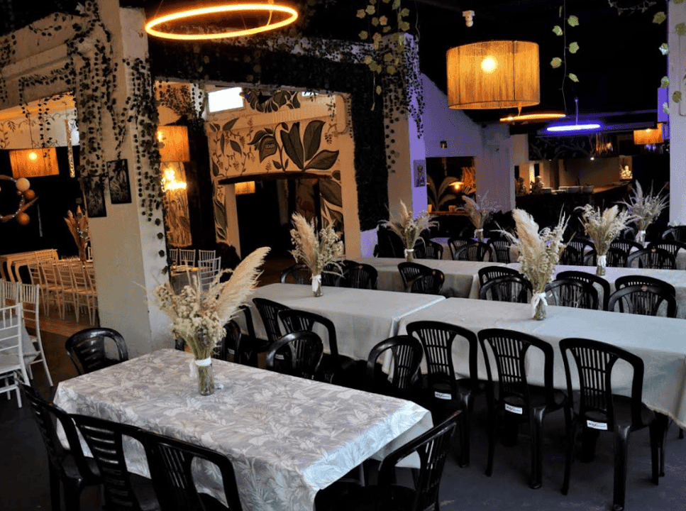 Salón interior con mesas montadas, manteles florales, sillas negras y murales decorativos