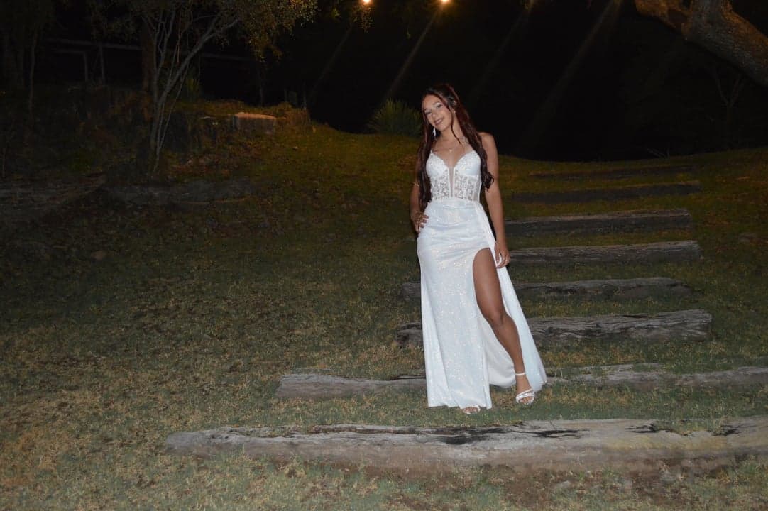Joven de vestido blanco posando en escalinata exterior entre árboles de noche