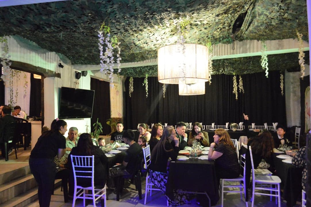 Invitados sentados en mesas con sillas Tiffany y decoración colgante de hojas y flores