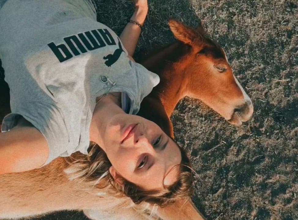 Angie, fundadora de África Eventos, recostada en el pasto junto a un potrillo